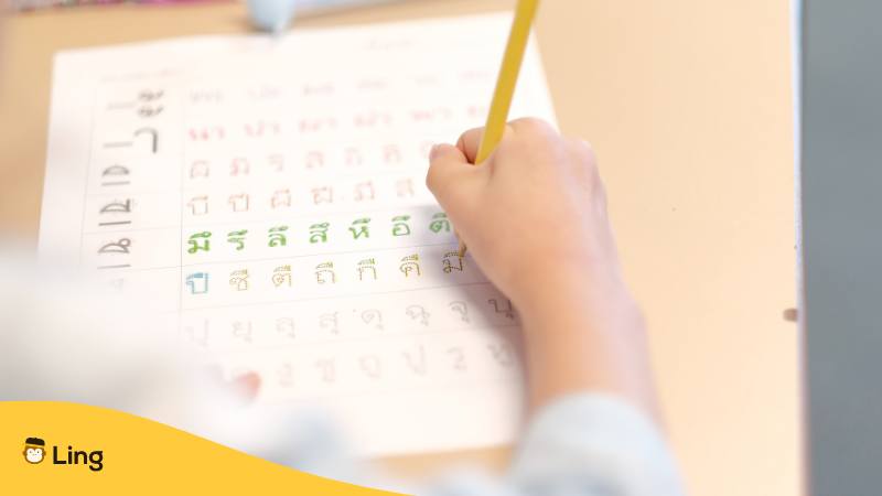 Hand eines Kindes schreibt die Buchstaben vom thailändische Alphabet mit Phonetik nach um es zu lernen