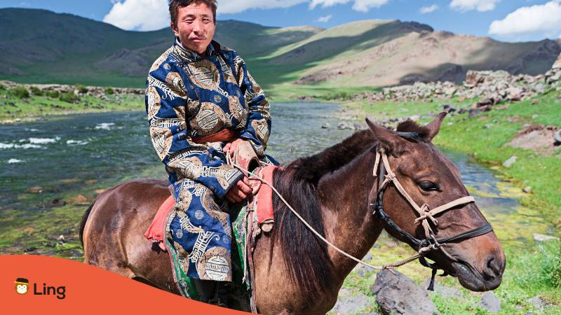Mongolischer Einheimischer in einem traditionellen Kostüm sitzt auf einem Pferd