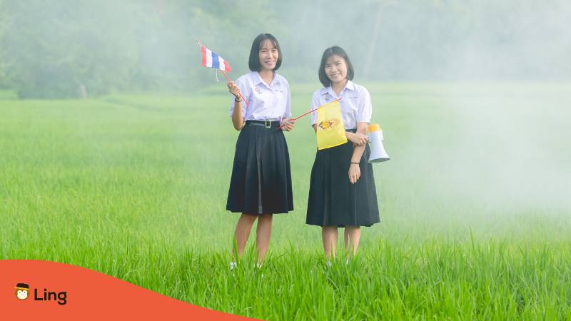 Thai Studentinnen stehen in einem Reisfeld mit thailändischen Flaggen