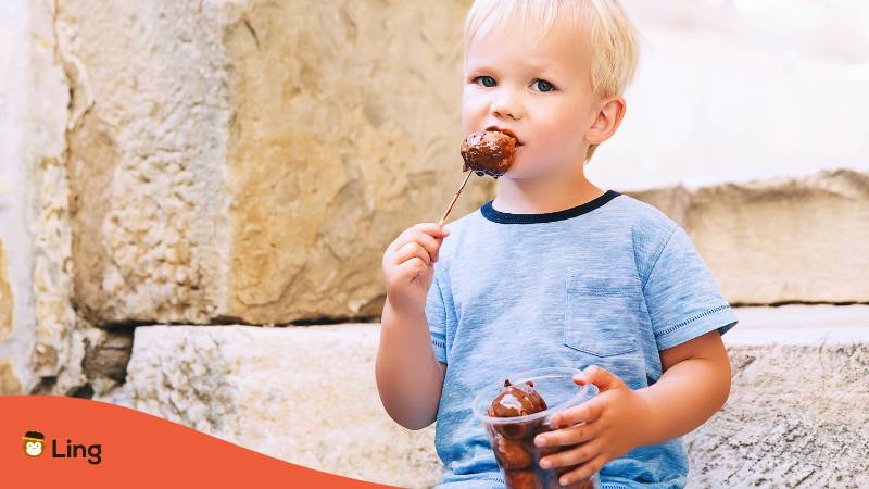 Blond boy eating Fritule dipped in chocolate in the streets of Croatia