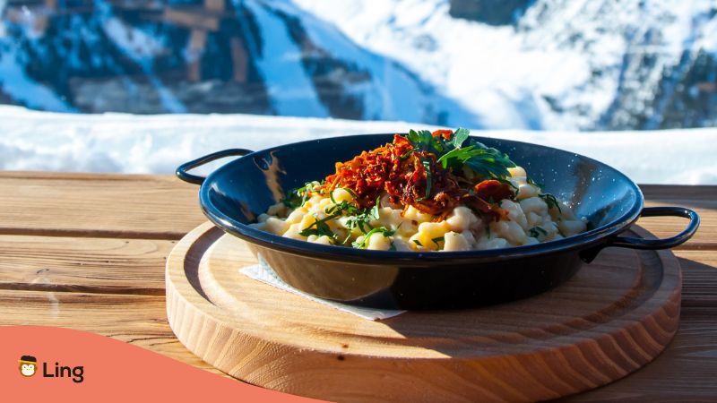 Pan with Southern German Food Käsespätzle in the background mountains with snow