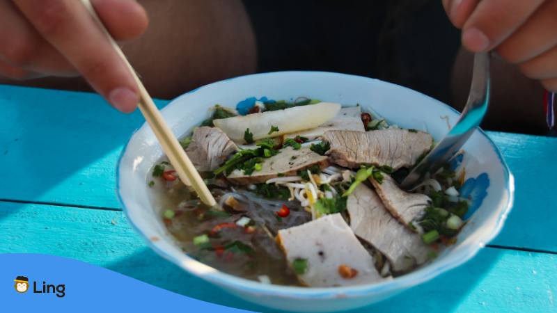 Hands holding chopsticks and asian soup spoon into a bowl with Vietnamese Soup Hu Tieu
