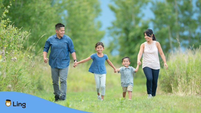 Filipino Family of four holding each other by the hand walking in a green meadow