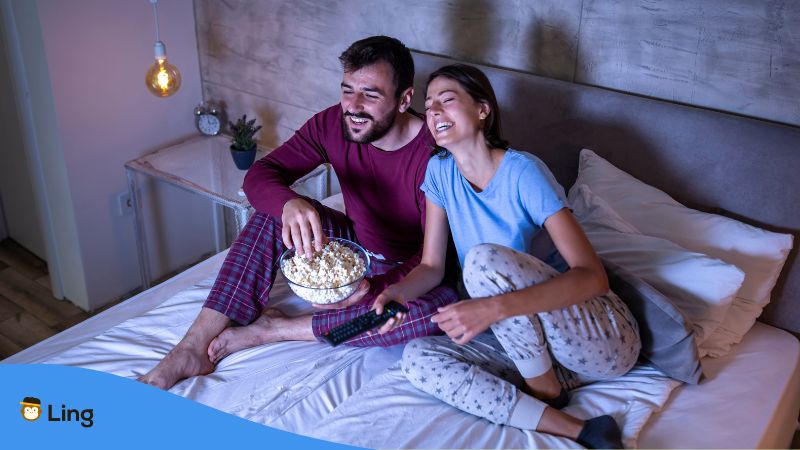 Paar sitzt auf dem Bett mit einer Schüssel Popcorn und streamt Malaysische Filme online
