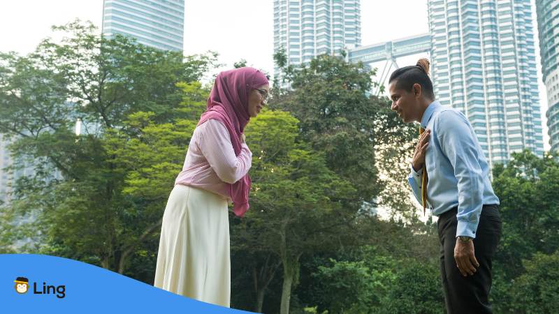 Frau im Kopftuch und Mann im Anzug verbeugen sich leicht und halten die rechte Hand an ihr Herz um sich geschäftlich zu begrüßen in Malaysia