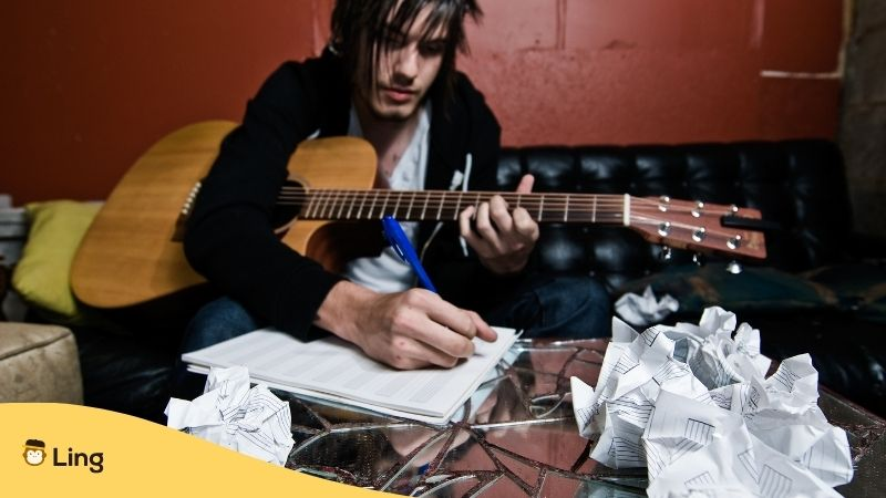 Musiker mit Gitarre schreibt Lieder auf einem Sofa