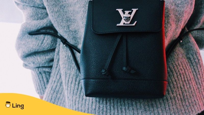French Luxury Brands. Black Lous Vuitton women's satchel being worn by a woman in a grey woollen top.