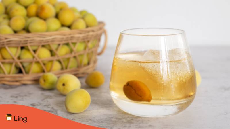 Basket with plums and a glass filled with icecubes a plum and yellow japanese plum wine