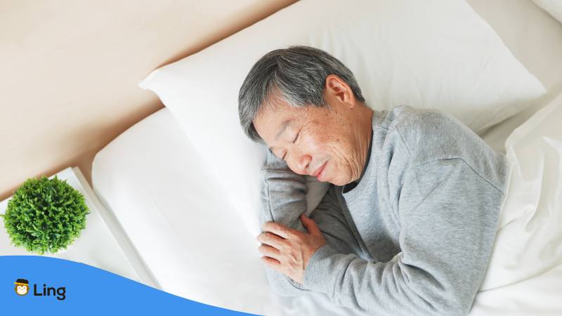 Japanischer Mann schläft friedlich in einem Bett, nachdem er "Schlaf gut" auf Japanisch gesagt hat