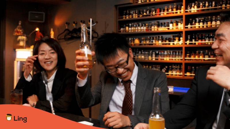 Japanese woman and two men sitting together saying cheers in Japanese and enjoying a beer