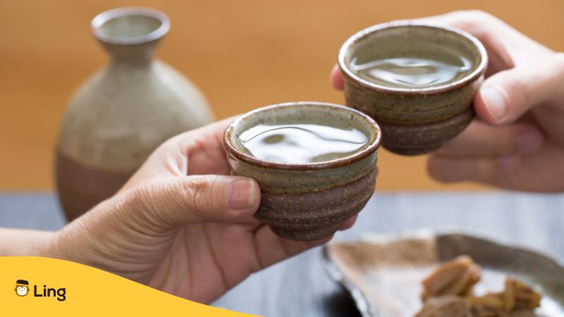 Two hands cheering with a cup of sake showing the Japanese Proverb that Sake shows true feelings.