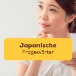 Asiatische Frau sitzt an einem Schreibtisch und hält mit einer Hand einen Notizblock und lernt japanische Fragewörter