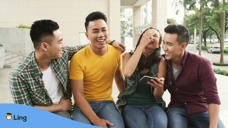 A group of young Asian men and a girl sitting together in an urban street and laughing at jokes in Cantonese.