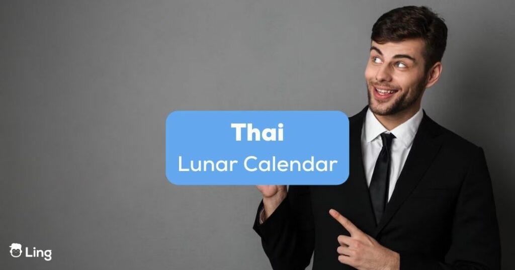 A man in a black suit pointing at the Thai lunar calendar.