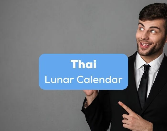 A man in a black suit pointing at the Thai lunar calendar.