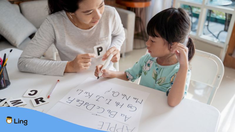 A Young Student And A Teacher Discussing How The Thai Alphabet Differs With English Alphabet.