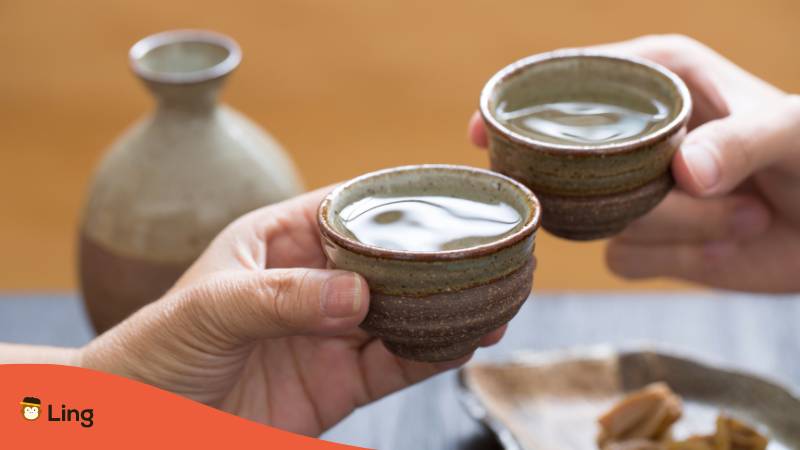Zwei Hände stoßen mit japanischem Reiswein Sake an Geschichte des Anstoßens in Japan