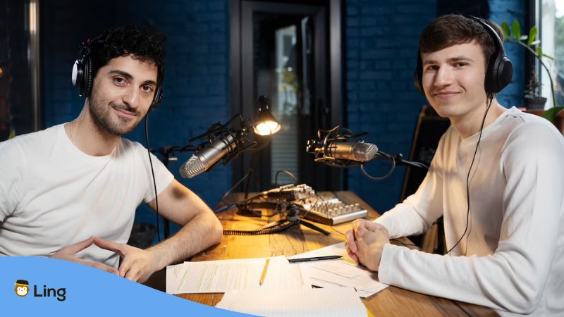 Two male podcast hosts inside a podcasting studio with a wooden table.