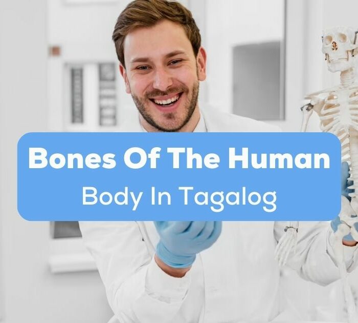 A smiling male Orthopedic doctor holding a skeleton model inside his clinic behind the bones of the human body in Tagalog texts.