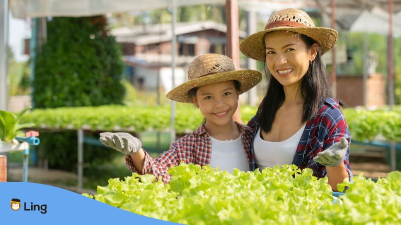 A photo of a mother and her daughter outdoors showing their fresh produce speaking gardening terms in Thai.
