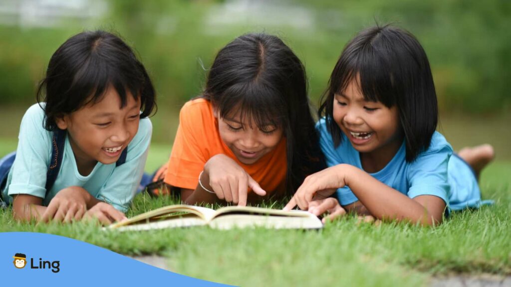 A group of children lying and reading Tagalog rhyming words on a grass field.