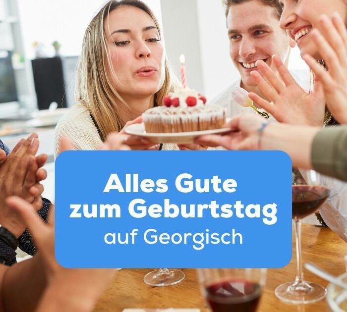 Blonde Frau bläst Kerzen auf Geburtstagstorte während ihre Freunde Alles Gute zum Geburtstag auf Georgisch wünschen