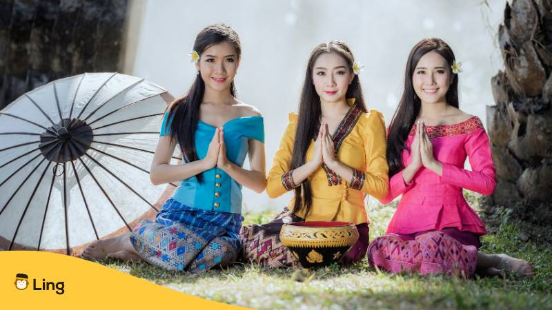 Drei laotische Frauen sitzen auf dem Boden in traditioneller Kleidung und machen den Nop um sich auf Laotisch zu bedanken