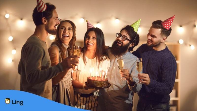 Brünette Frau feiert mit Freunden ihren Geburtstag in Georgien mit Partyhüten und Torte während ihre Freunde Alles Gute zum Geburtstag auf Georgisch singen