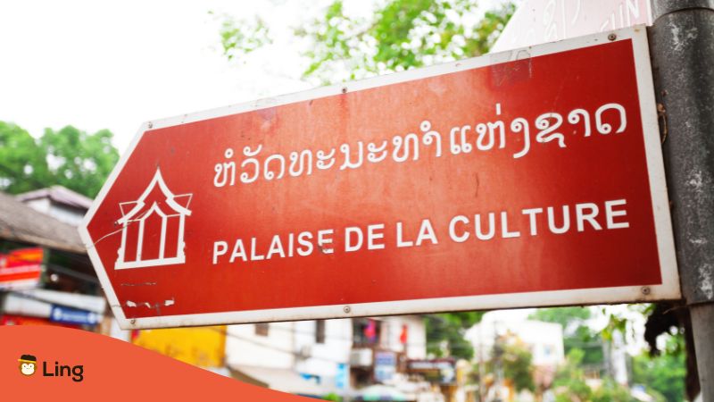Straßenschild in Vientane Laos, in laotischer Schrift und auf Französisch das zum Palast der Kulturen zeigt
