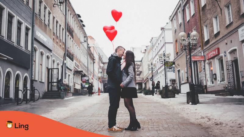 Paar in Georgien steht auf der Strasse mit Herzluftballons und küsst sich und sagt sich Ich liebe dich auf Georgisch