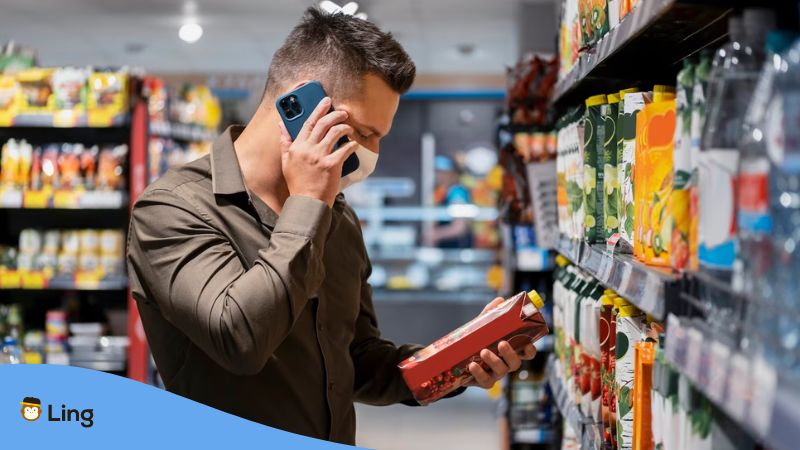 A photo of a man reading the nutritional components of a juice inside a convenience store while using his phone.