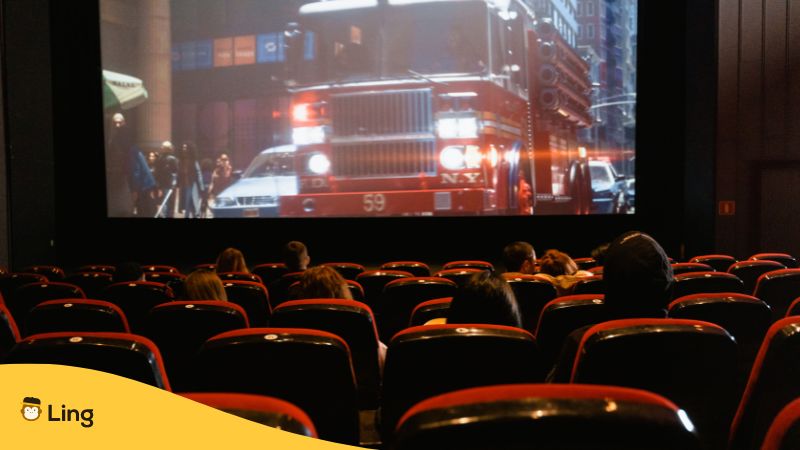 people watching a movie inside a cinema showing a scene with a red truck on a street