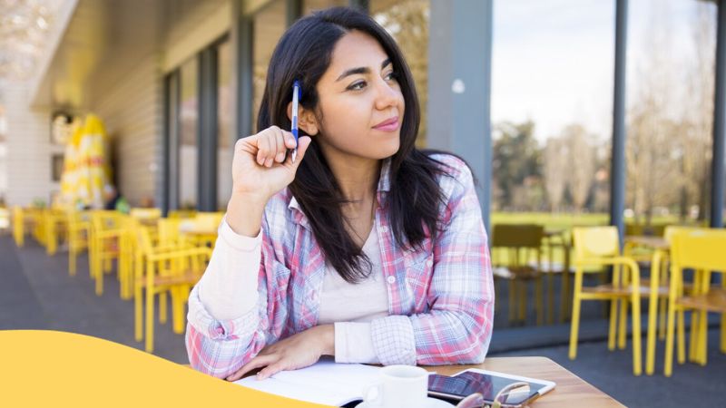 apps to learn Latin - A photo of a woman holding a pen, sitting outside a café