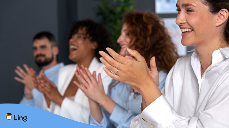 A photo of happy people clapping as a sign of appreciation and compliments in Lithuanian.