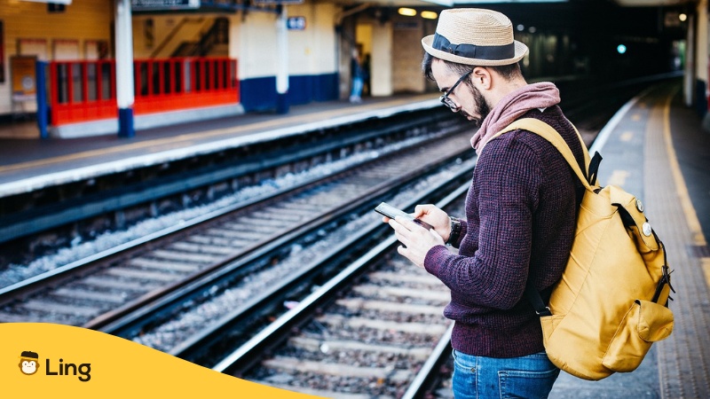 Man on train station with phone - Language learning apps for travelers Ling app