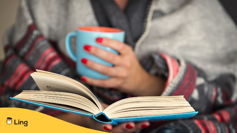 woman with red nail polish holding a book and reading while holding a mug