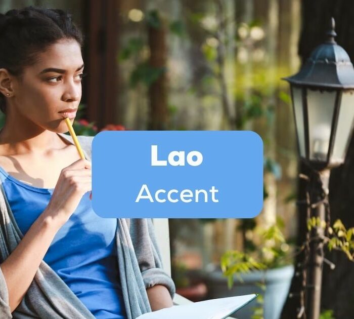 A photo of a girl holding a pencil and a notebook outside a house behind the Lao Accent texts.