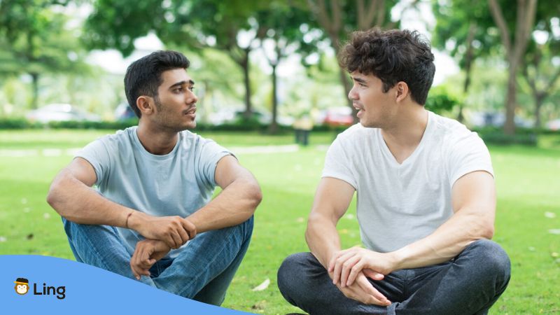 A photo of two male friends with different Lao accents talking while sitting on a grass field.