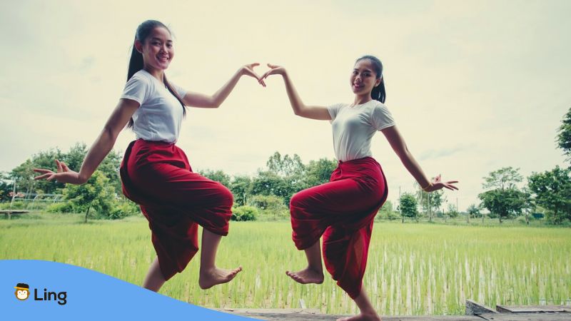 A photo of two girls dancing in front of a rice field as part of Laos traditions and rituals.