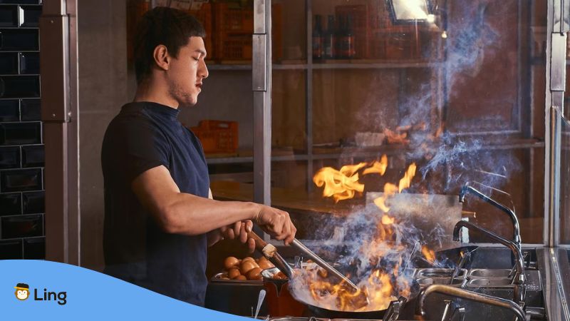 A photo of a man cooking using a wok with blazing fire.