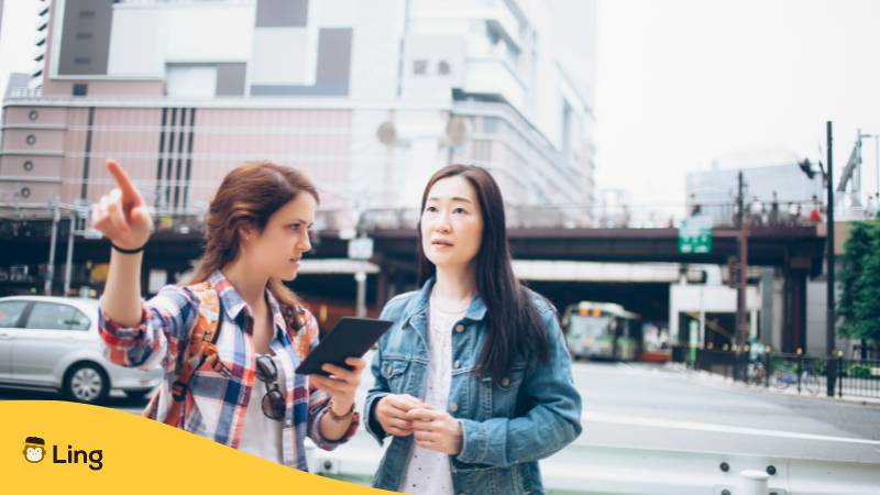 Frau hält Handy in der Hand um mithilfe der Ling-App eine Einheimische auf Kantonesisch nach dem Weg zu fragen