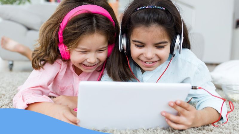 apps for learning English for kids - A photo of two happy kids using a tablet with their headphones on