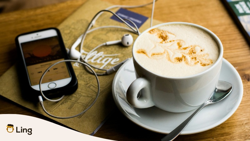 Phone with headphones playing audio and coffee  - Ling app Language learning apps with podcasts 