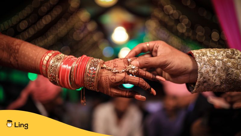 bride's arm and hands covered in accessories and tattoos and the groom's hand putting a ring on her finger