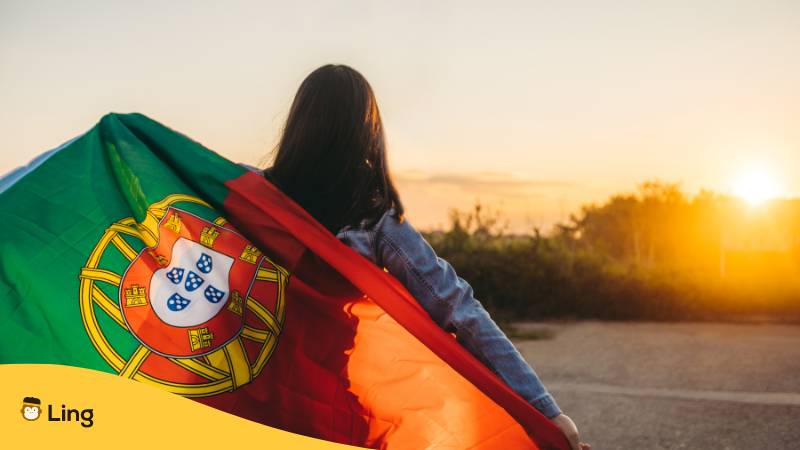 Portugiesin hält portugiesische Flagge und schaut sich Sonnenuntergang an. 