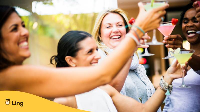 Frauen stoßen bei einer Feier gemeinsam mit Cocktails an und sprechen einen toast auf Italienisch aus