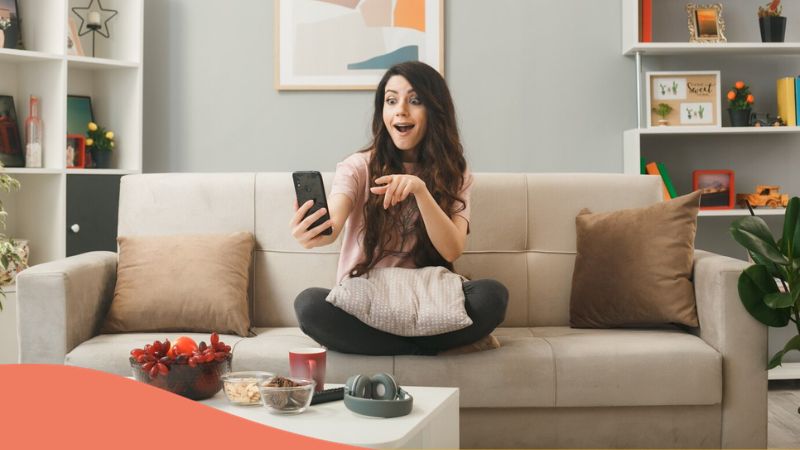 apps to learn Romanian - A photo of a surprised looking girl using her phone while sitting on a couch