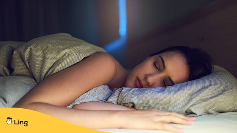 Braunhaarige Frau liegt entspannt im Bett und schläft, nachdem sie eine Gute Nacht auf Lettisch gewünscht hat