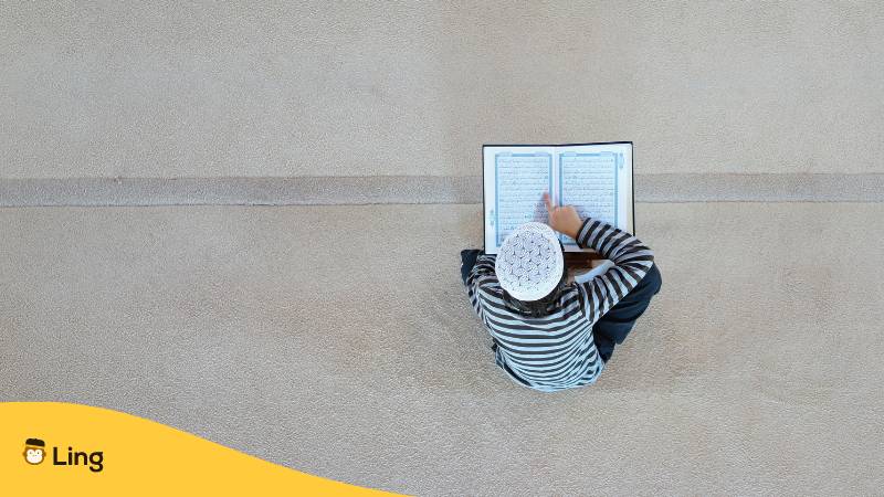 Muslimischer Junge sitzt auf Treppe und liest im Koran auf Arabisch