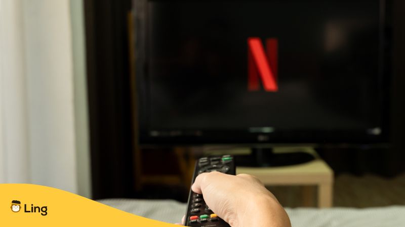a hand holding a remote control pointing on TV with Netflix on